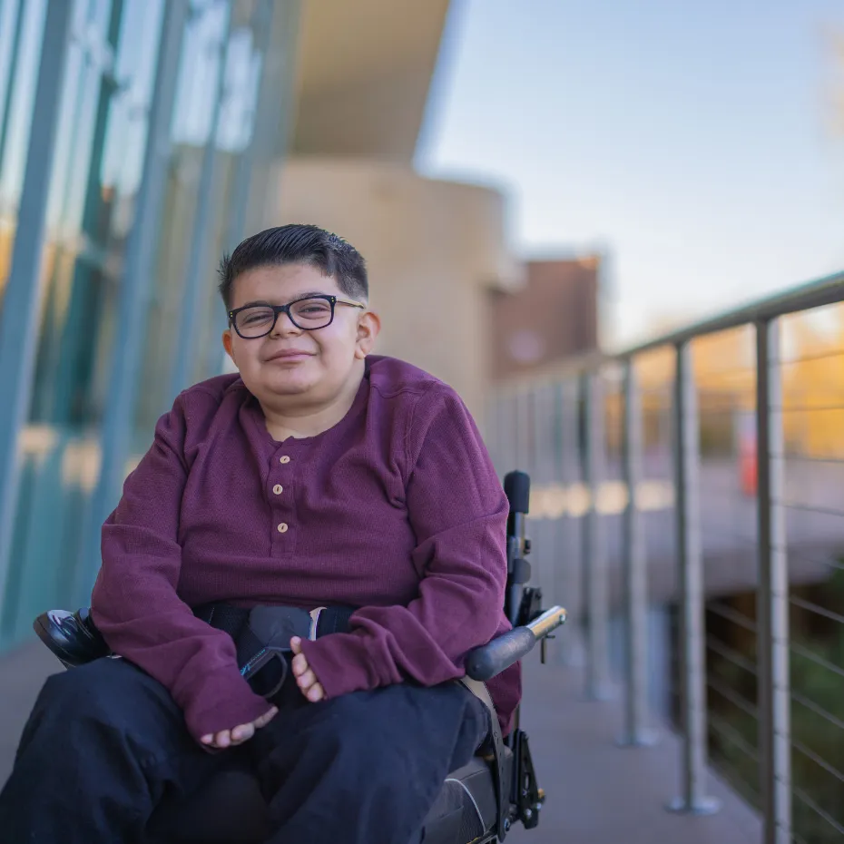 A young Onboard Supports participant smiling outside in their wheelchair